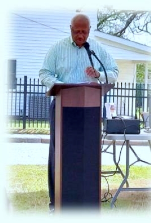A man in a light shirt and dark pants speaking at a podium.