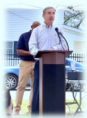 A man in a light shirt and dark pants at a podium speaking.