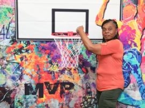 Ladies in a orange shirt standing with a basketball hoop.