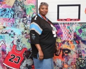 Ladies in a black, white, and blue shirt standing with a basketball hoop.