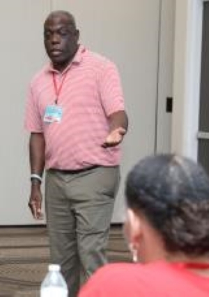 Man in a pink shirt speaking to an audience.