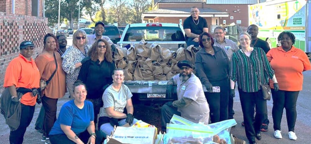 A group of people stand around a truck full of bags of food that are going to be distributed to community members.