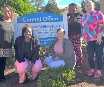 A group of women wearing pink standing around the Washington Housing Authority sign.