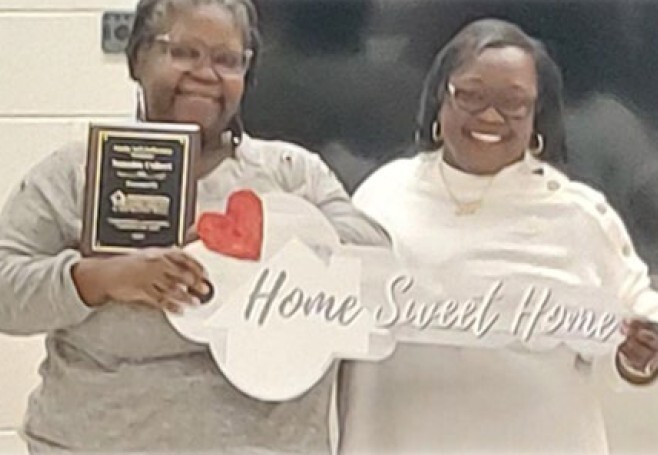 Natasha Colbert holding a plaque and a a sign that says Home Sweet Home.