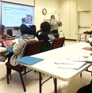 People sitting at tables listening to a person speaking.