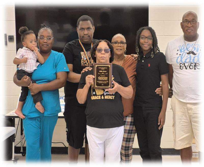 Millie Ebron holding an award with six other family members standing behind her.