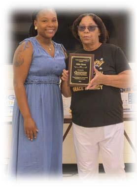 FSS Graduate Millie Ebron holding her award standing with another smiling woman.