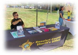 A police officer sitting at a table with a Beaufort County Sheriff's Office table cloth. 