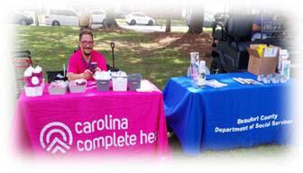 A man sitting at a table with a Carolina Complete Health table cloth, next to a table with a blue table cloth.