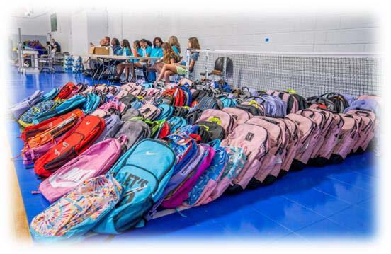 Many backpacks laid out in lines on the floor.