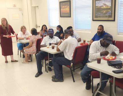 People are gathered around a dining area, sitting at tables, and eating food.