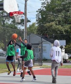 A different ground of people are playing basketball and fighting for possession of the ball.