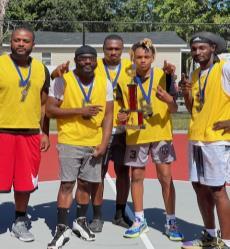 Four basketball players bend down low to fight for possession of the ball.