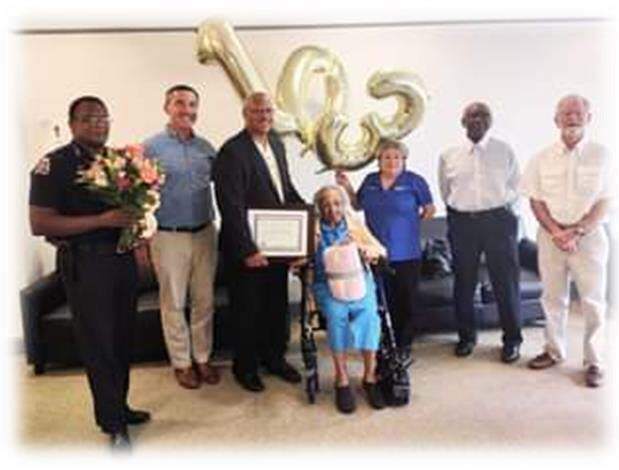 A police office and various other city officials stand behind Ms. Lillian Boyd holding balloons that read 103. 