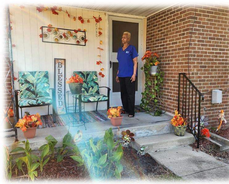 Patricial Little stands on her porch and shows off her winning yard of the month.