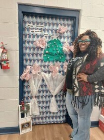 A woman stands in front of a decorated door with her hand on her hip.