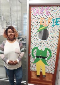 A woman holding her hands together and standing in front of a decorated door.