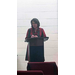 A woman in plaid speaks from the podium. 