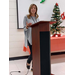 A woman with shoulder length hair stands behind a podium and addresses the room of people. 