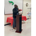 A man stands behind a podium with an arm raised and addresses the room of people. 