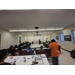 The view from the back of the classroom. A group is sitting at tables while listening. 