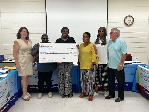 A group of individuals gather around a large oversized check.