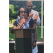 A woman at a podium speaking while a man stands in the background.