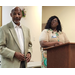 A man and a woman standing inside and the woman is standing behind a podium.