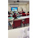  Nine kids sitting at tables watching a video on the screen at the front of the room. 