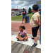  A boy and man standing, and a girl sitting on the ground by the dock. 