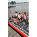  Four kids sitting, and one standing in the boat. 