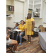  A woman in a yellow dress stands and smiles for a picture next to two people sitting at a table. 