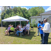  People sitting under a tent, and people standing next to it. 