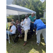  People standing under a tent with a guy bending over helping someone. 