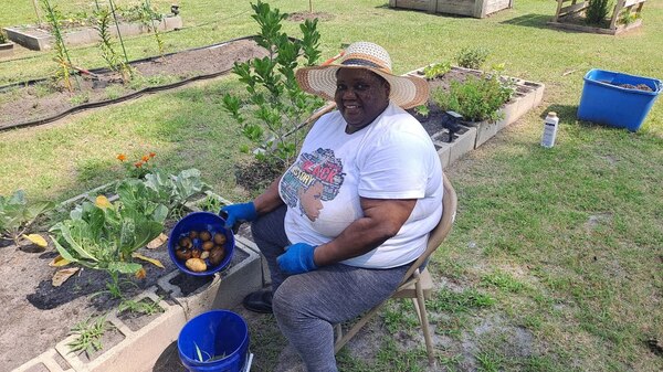 A woman sitting and smiling with a bucket of potatoes.