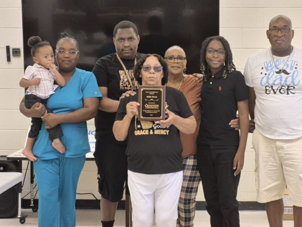 A woman stands with a plaque surrounded by family.
