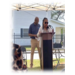  A woman speaking at a podium with a man standing behind her. 